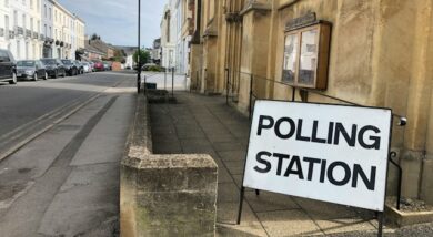 Sign on the Pavement shows 'Polling Station' against background of town centre.