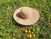 A straw hat sits on a vibrant green grass field, adorned with dandelions, under the summer sun.