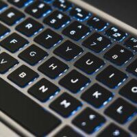 A detailed view of a backlit laptop keyboard with glowing blue lights.